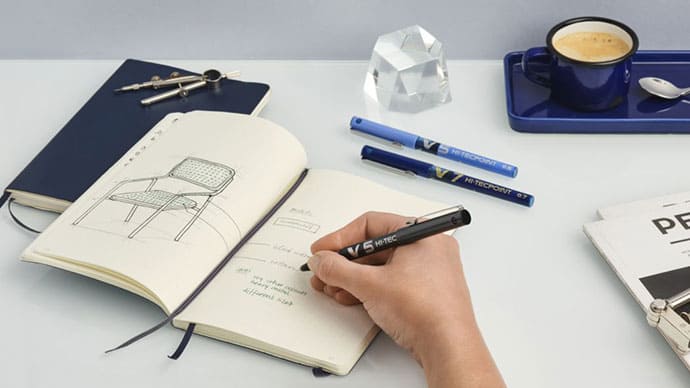 Mano escribiendo y dibujando en un cuaderno con Pilot rotulador negro V5