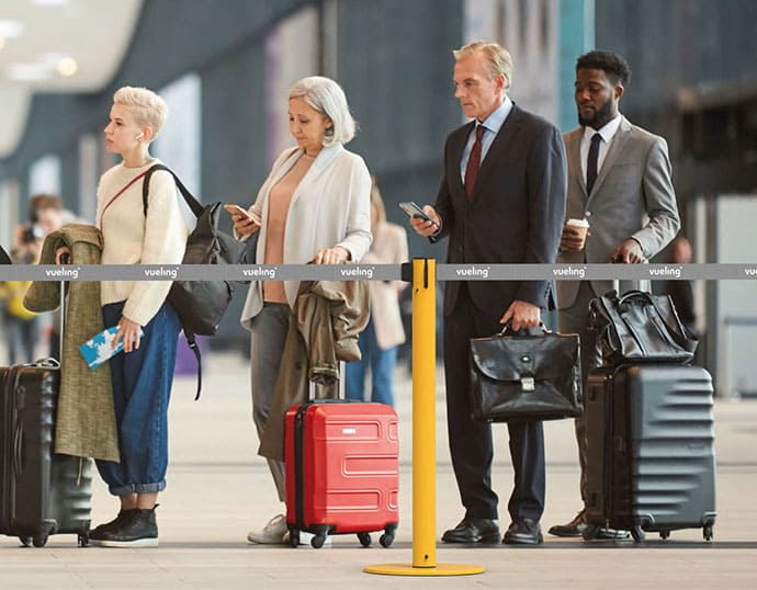 Gente esperando en una fila tras un poste separador con cinta de Vueling