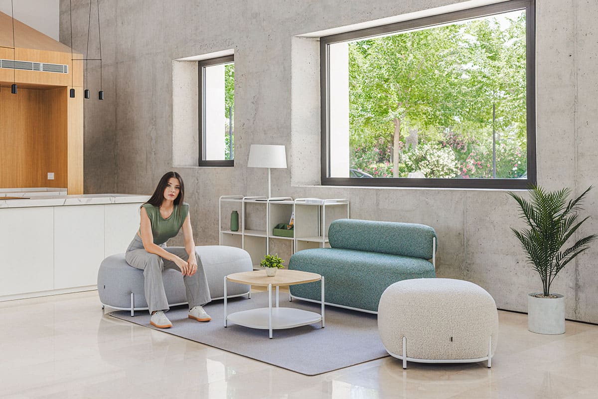 Colección Globb Actiu: sofás modulares con patas finas y formas redondeadas Modelo sentada en un asiento, rodeada de una muestra completa de la colección Globb Actiu de diseño orgánico