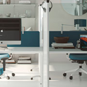 Mampara de metacrilato transparente colocada sobre divisoria de sobremesa tapizadas en color azul para oficina con muebles de diseño