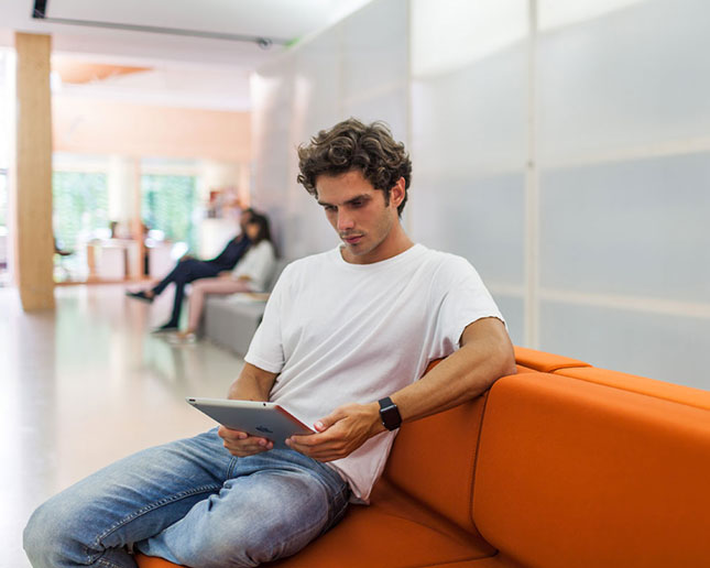 Hombre sentado en sofá modular Longo Actiu naranja en sala de espera moderna