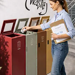 Mujer desechando papel en papeleras de colores para identificar el reciclaje