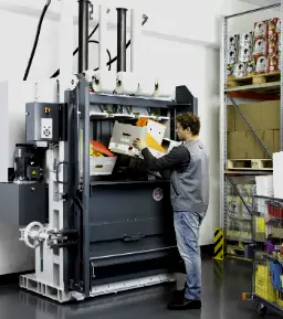 Trabajador en almacén industrial llenando de cartón una prensa compactadora hidráulica para reducir su volumen
