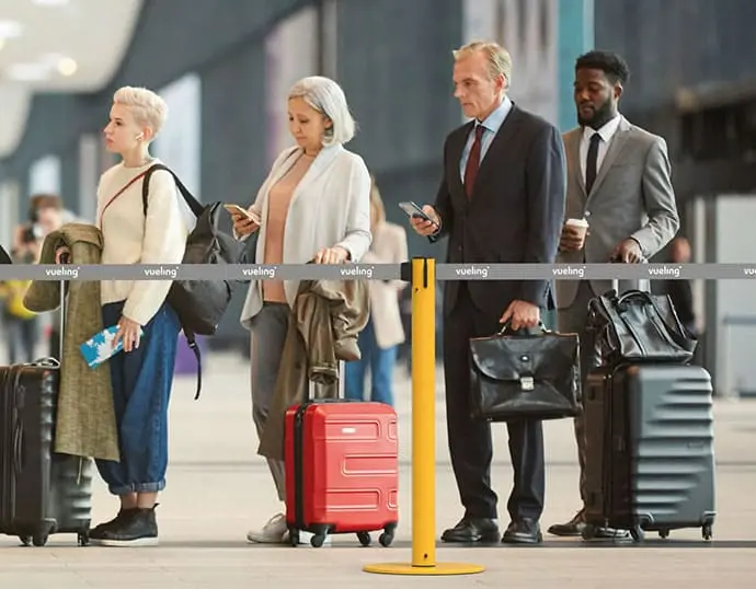 Gente esperando en una fila tras un poste separador con cinta de Vueling