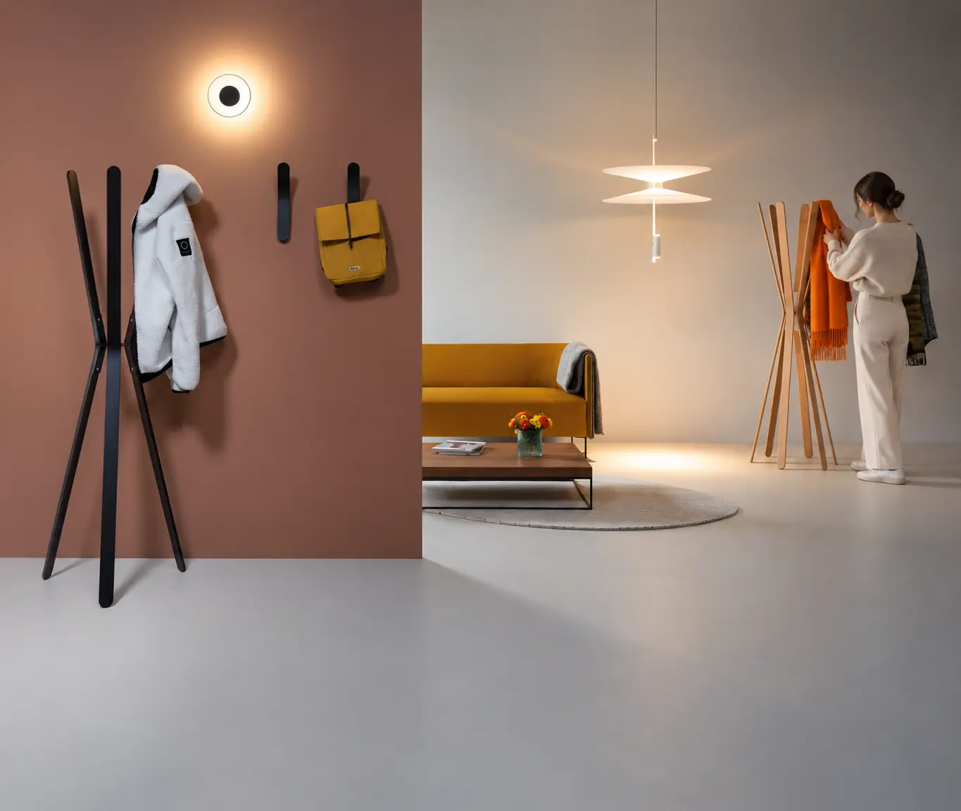 Perchero de pie integrado en un espacio contemporáneo y minimalista, mostrado en una escena de uso real con una persona colocando una prenda. Un ambiente cálido y elegante que destaca la funcionalidad del perchero y su capacidad para integrarse en oficinas, recepciones, zonas de espera y espacios contract.