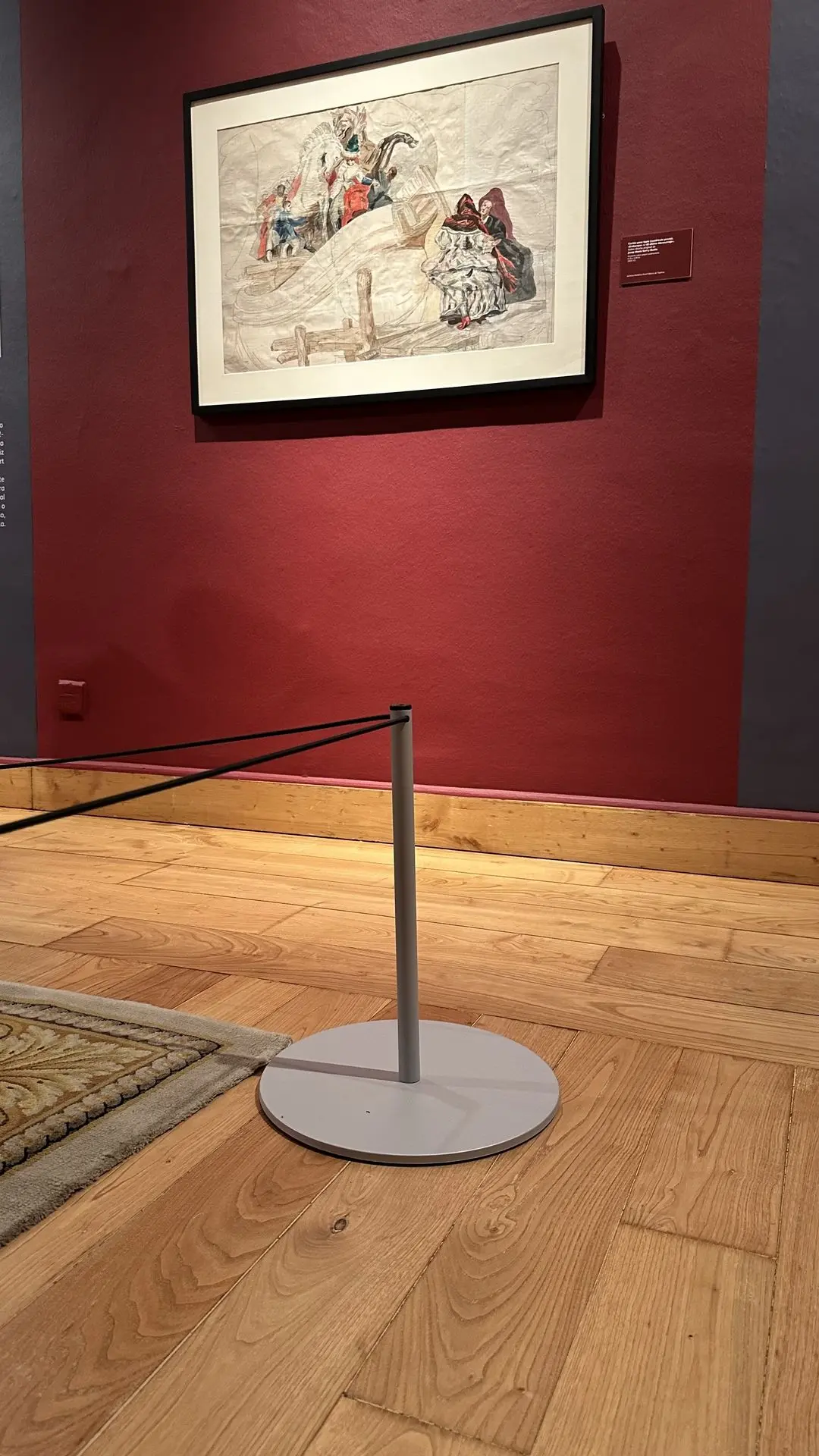 Poste Gallery Mini con cuerda elástica negra junto a una alfombra y un dibujo enmarcado en una sala de pared roja